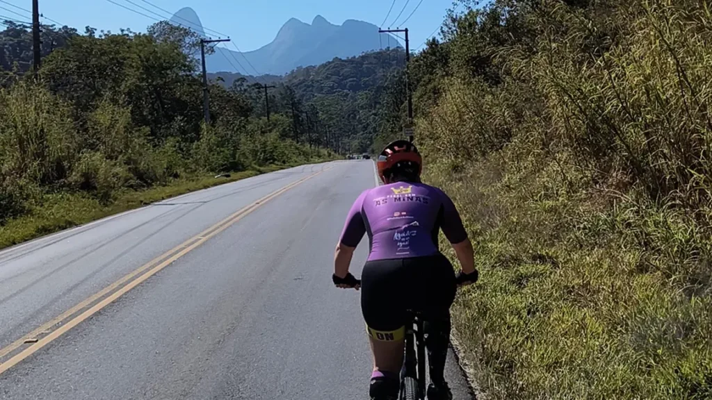 Integrante do grupo Pedal Kom As Minas pedala pela rodovia Teresópolis–Friburgo com a formação rochosa Mulher de Pedra ao fundo, na Região Serrana do Rio de Janeiro.