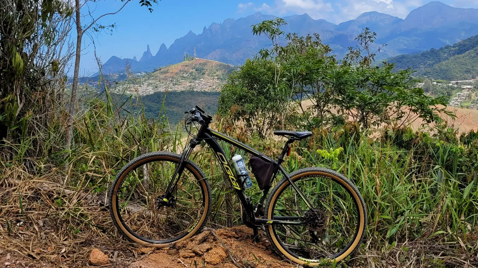 Bicicleta em trilha de terra com vista para a Serra dos Órgãos, em Teresópolis, destacando o potencial da região para o turismo de natureza e o mountain bike.