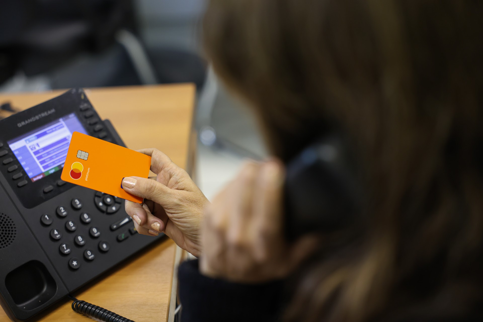 Pessoa idosa fala ao telefone enquanto segura um cartão de crédito, ilustrando os riscos de golpes financeiros.